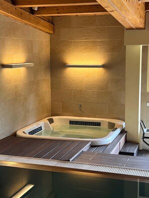 A spa room with a freestanding bathtub, wooden ceiling beams, and wall-mounted lighting.