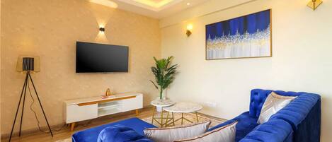 A modern living room with a blue sofa, a flat-screen TV, a white console, a small round table, and a floor lamp.