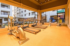 A gym with treadmills, elliptical machines, and a stationary bike, with a view of a residential area through large windows. - The Pearl Residence - Moonvalley (Nairobi)