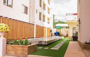 A courtyard with a water feature, a children's slide, and a staircase leading to an upper level. - The Pearl Residence - Moonvalley (Nairobi)