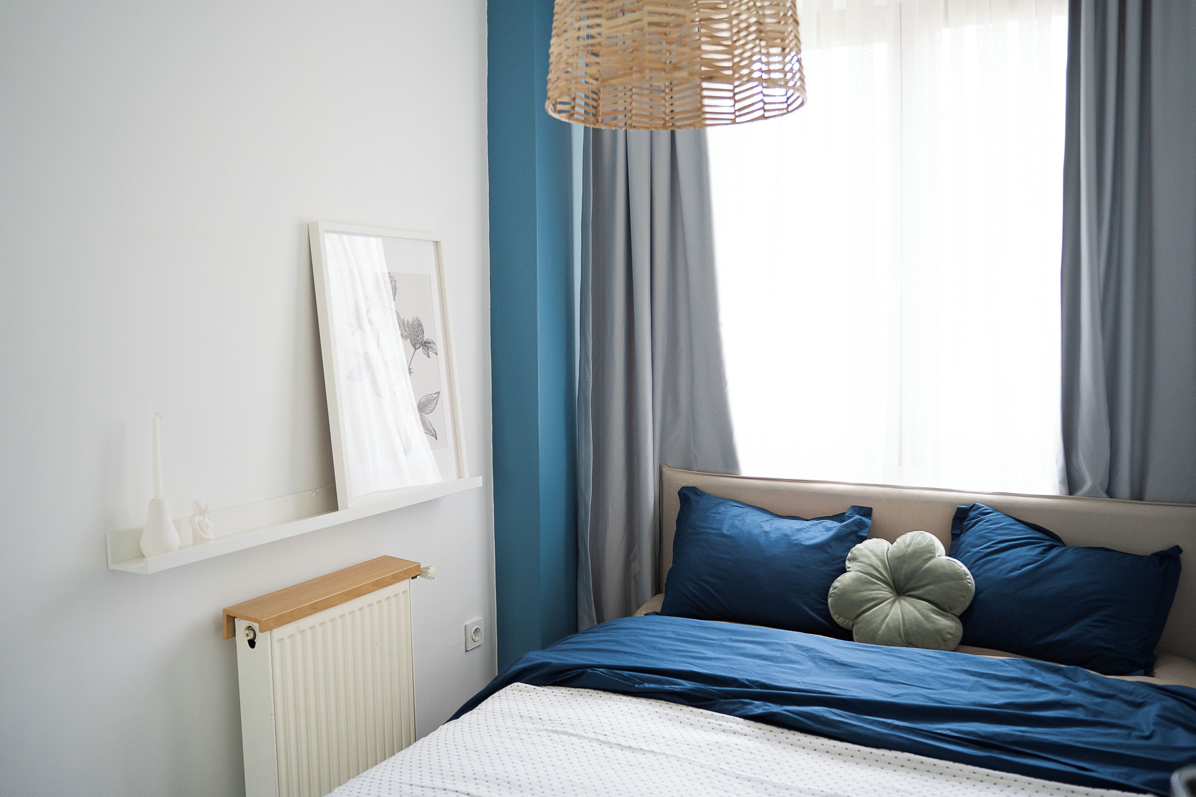 Ein Schlafzimmer mit einem Bett, einem Heizkörper, einem Regal mit Dekoration und einem Fenster mit Vorhängen.