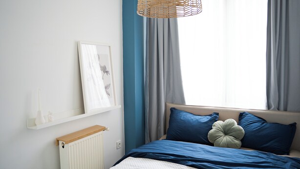 A bedroom with a bed, a radiator, a shelf with decorative items, and a window with curtains. - Stylish apartment with a separate bedroom near Taksim with AC (Istanbul)