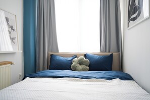Une chambre à coucher avec un lit, des rideaux, un radiateur et un tableau accroché au mur.
