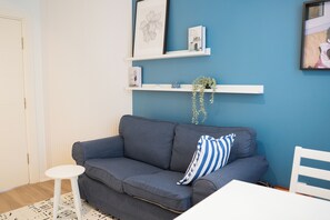 A room with a grey sofa, a white chair, a small white stool, and a blue wall with shelves holding books and a plant. - Stylish apartment with a separate bedroom near Taksim with AC (Istanbul)