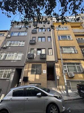 Un immeuble résidentiel à plusieurs étages, doté de balcons, de climatiseurs et d’un numéro de porte bien visible.