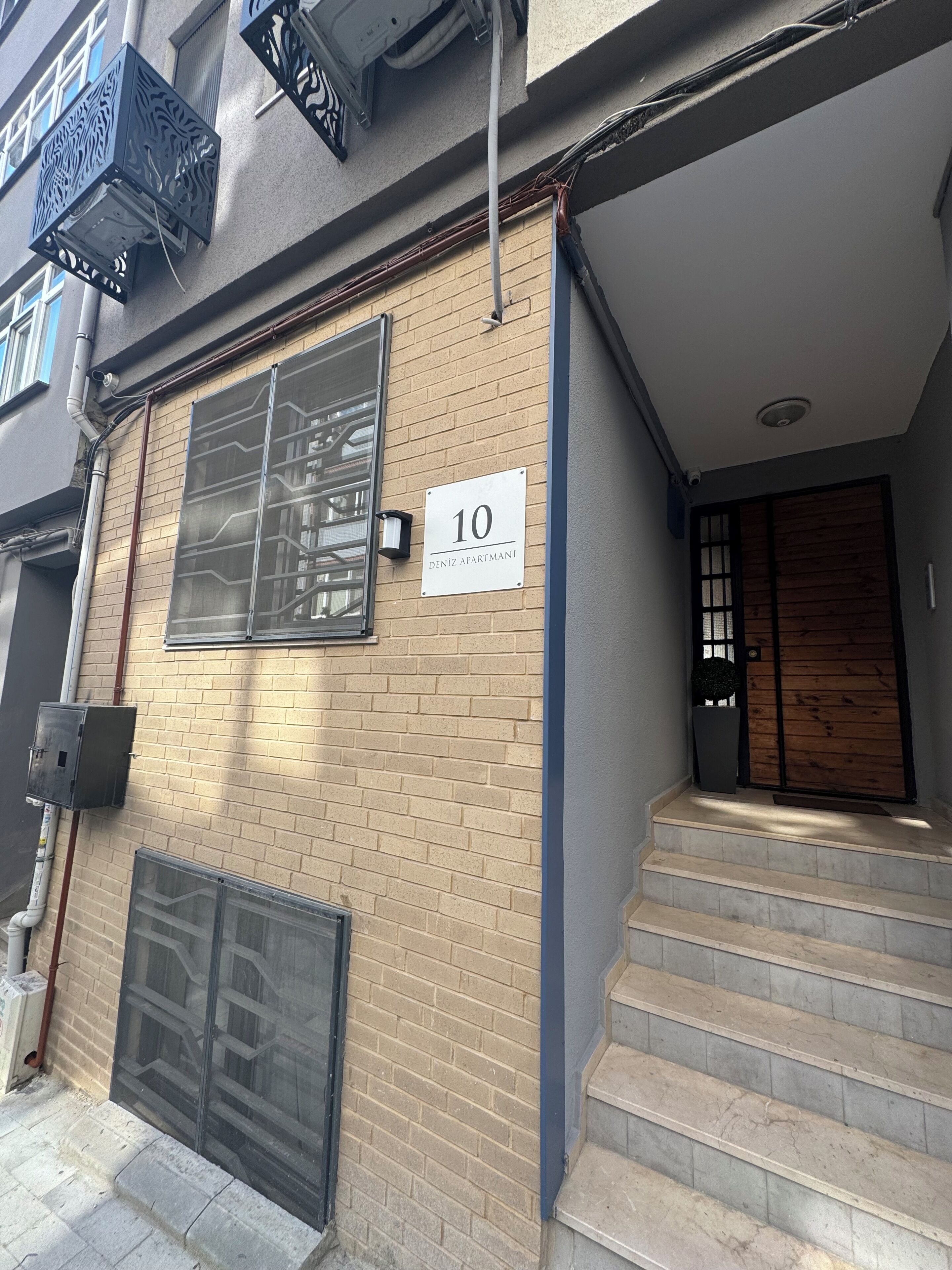 Ein Gebäude mit Ziegelverkleidung, einem Schild mit der Nummer 10, einem Fenster mit Metallgitter und einer Holztür.