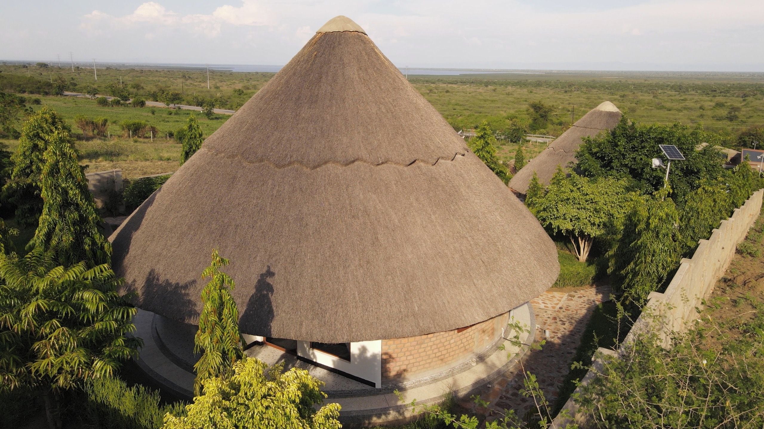 Estrutura com telhado cônico e base circular, rodeada por vegetação e uma paisagem plana ao longe.