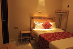 A single bed with a wooden headboard, a bedside table, and a red patterned bedspread.