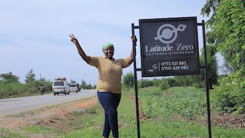 Eine Person steht neben einem Schild für Latitude Zero Cottages-Kikorongo mit Kontaktdaten.