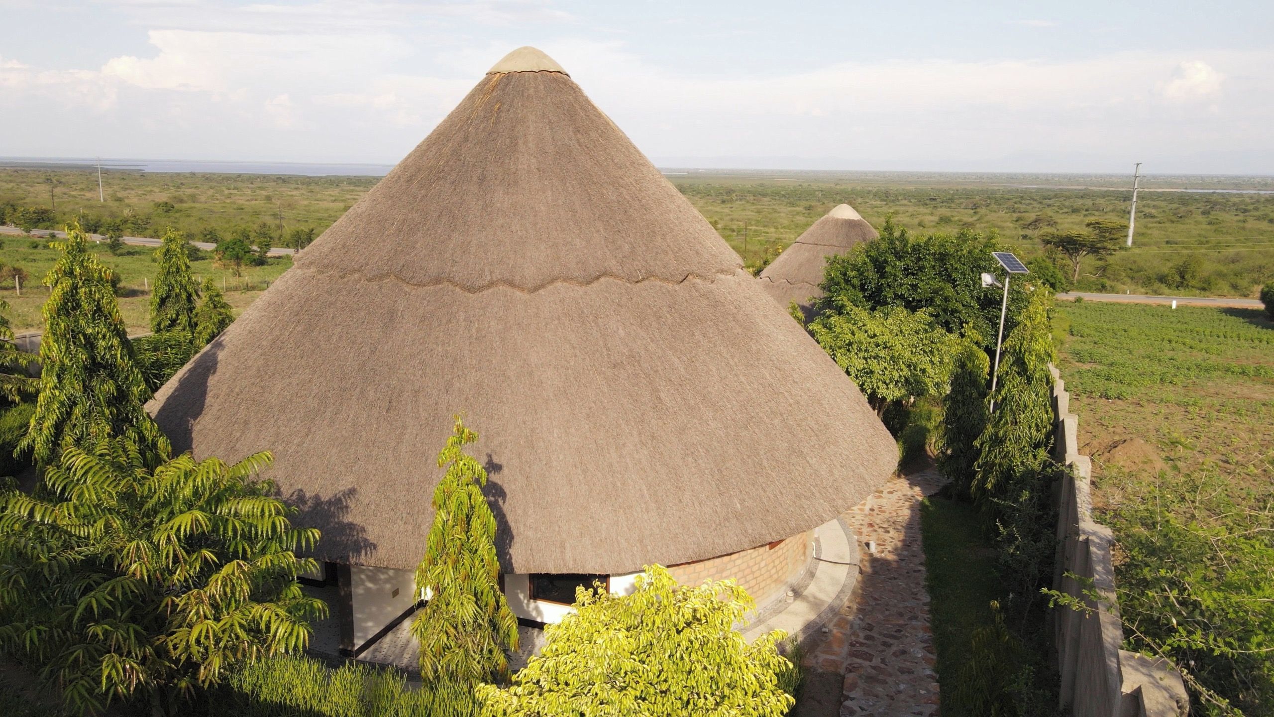 Casa com telhado de palha e um caminho de pedras que a leva, cercada por vegetação.