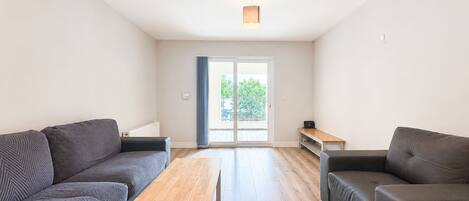Una sala de estar moderna con dos sofás, una mesa de centro de madera y un ventanal corredero que da a un área exterior.