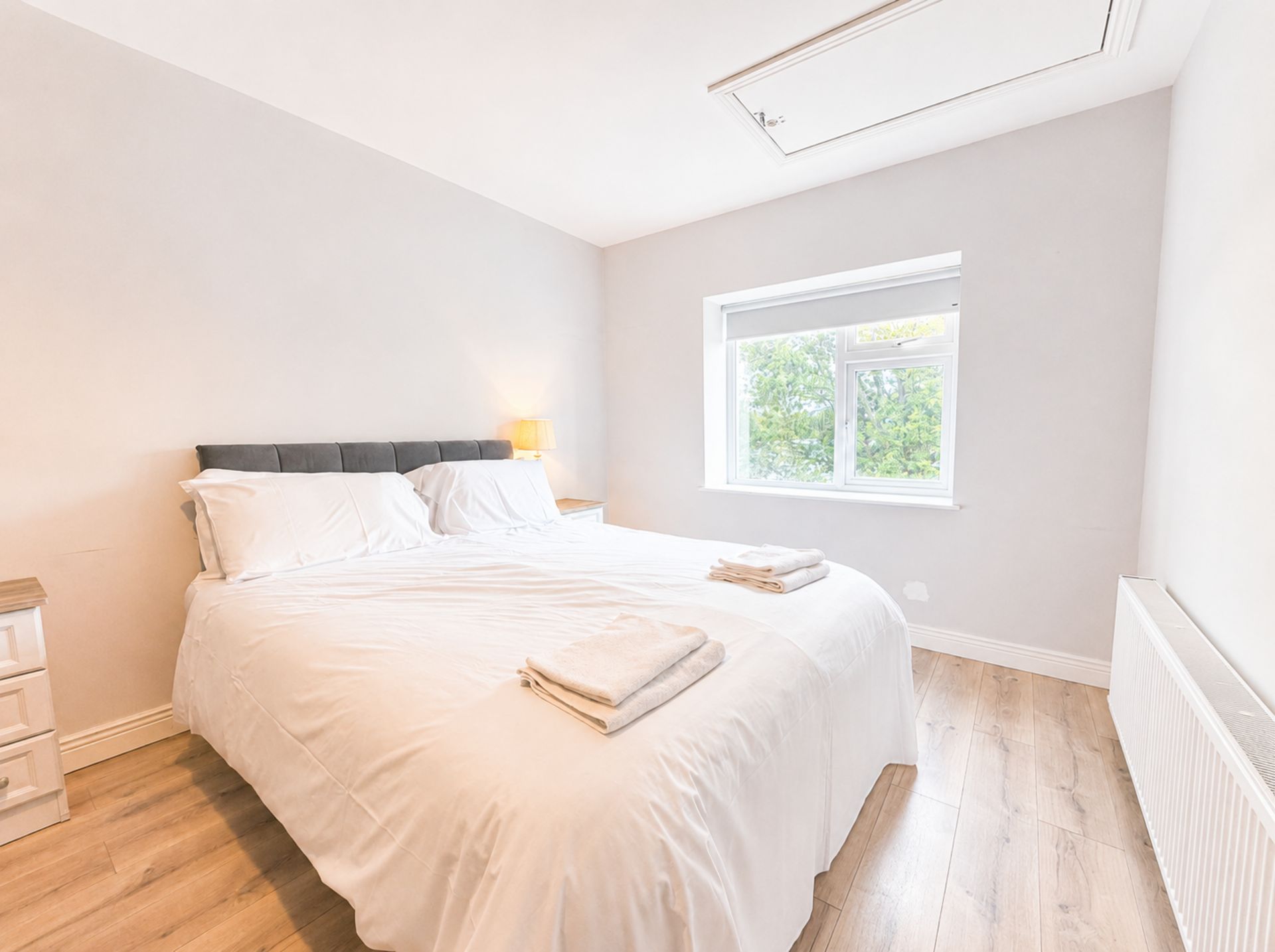 Un dormitorio con cama, mesitas de noche, ventana y radiador.