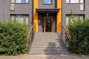 A modern building with a grey and orange facade, a central entrance with a door, and a staircase leading up to it. - Functional Studio near Pole Mokotowskie Workspace Smart TV (Warszawa)