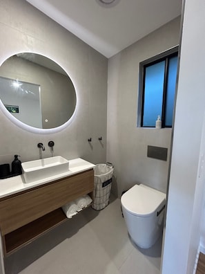 A modern bathroom with a white sink, mirror, and toilet.