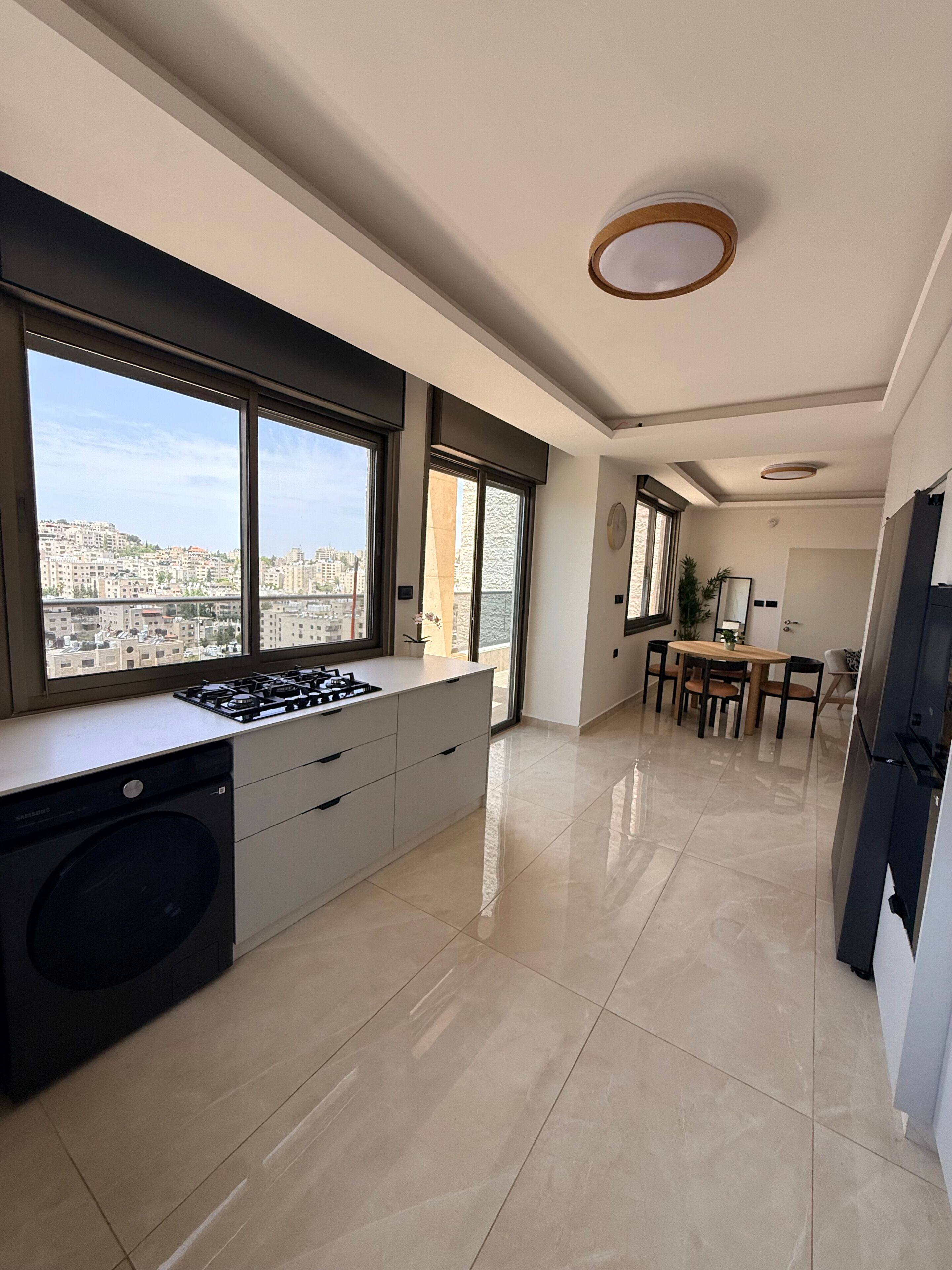 A modern kitchen with a built-in washer, large windows, and a dining area with a view of the city.