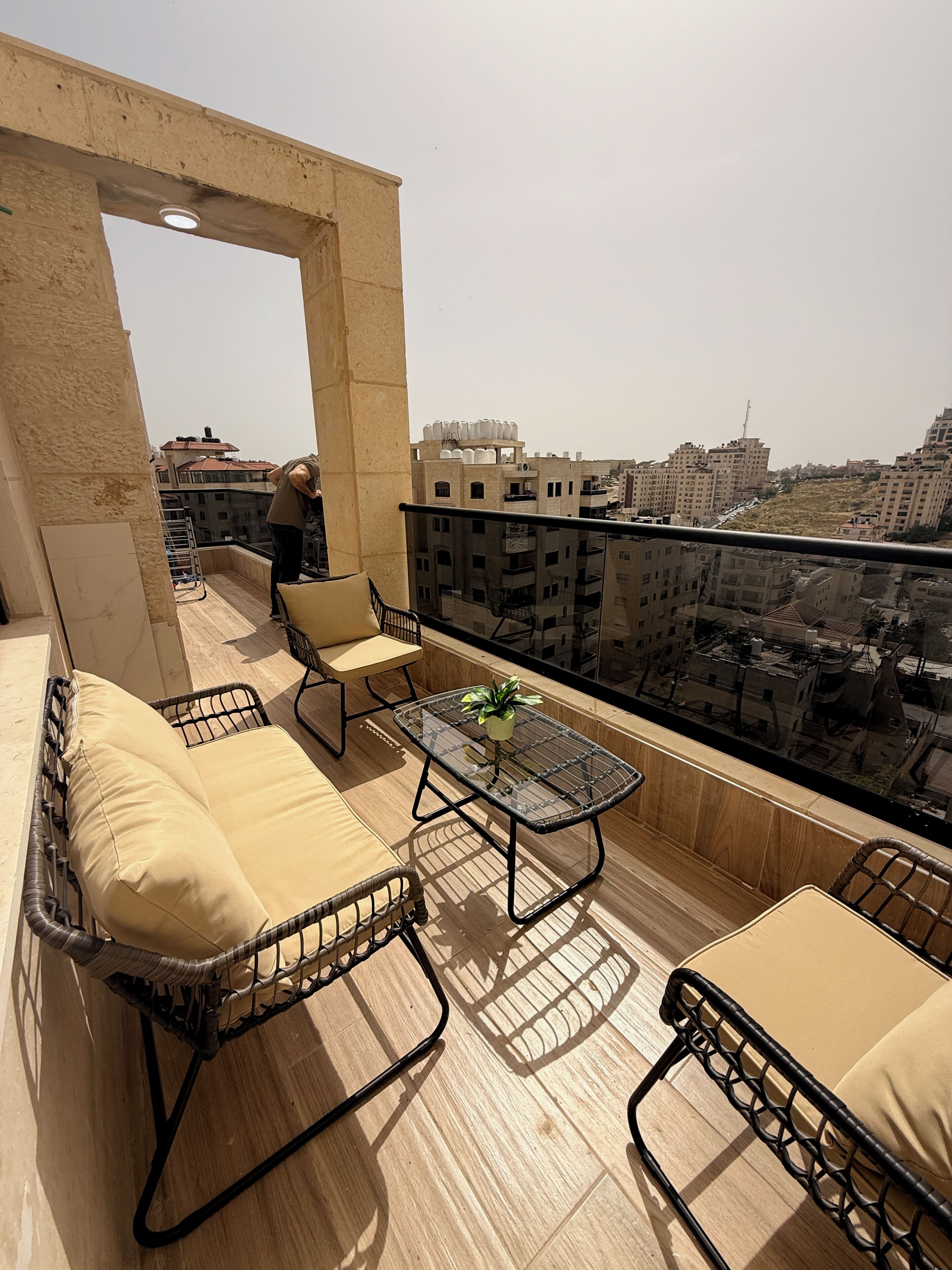 A balcony with wicker furniture, a glass table, and a view of the cityscape.