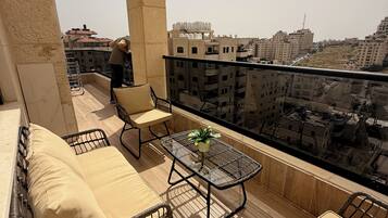 A balcony with wicker furniture, a glass table, and a view of the cityscape.