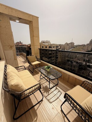 A balcony with wicker furniture, a glass table, and a view of the cityscape. - 3-bedroom apartment in beautiful Masyon in Ramallah (Ramallah)