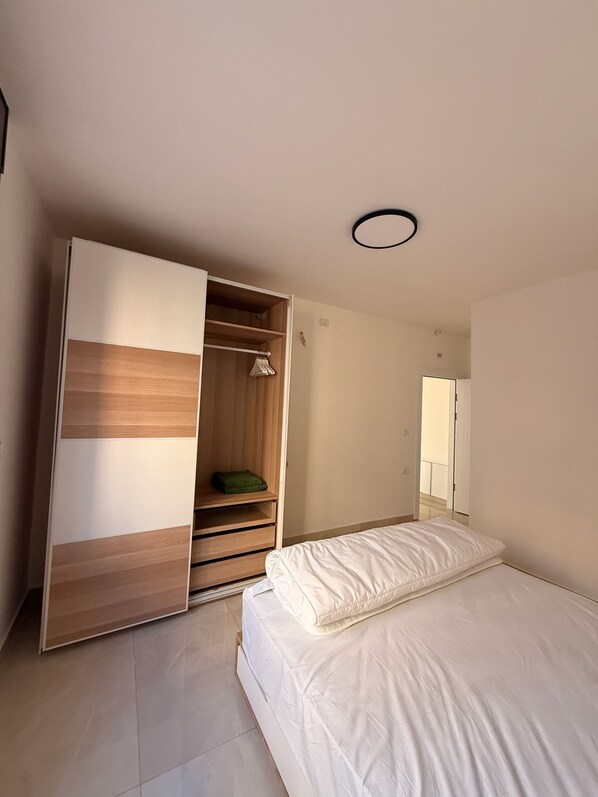 A bedroom with a bed, a wardrobe with a mirror, and a door leading to another room.