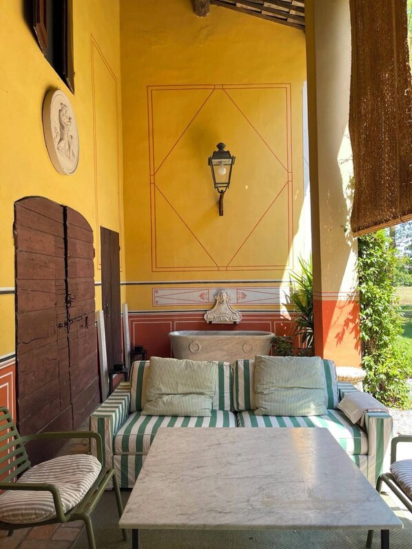 A sunlit outdoor seating area with a table and chairs, a decorative wall with a geometric pattern, and a hanging light fixture.