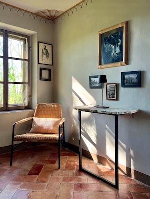 A room with a wicker chair, a small table, and framed pictures on the wall. - Villa Leopardi - A luxury guesthouse in the Parma countryside (Emilia-Romagna)