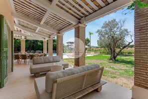 A covered outdoor seating area with sofas and a dining table, overlooking a pool and garden. - LUXURY BASTIDE WITH WALKING DISTANCE TO LA MOUTTE BEACH (Saint-Tropez)
