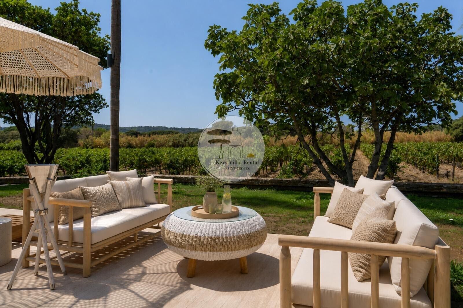 An outdoor seating area with a round woven table, two sofas, and a decorative sign.