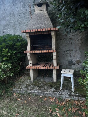 A brick-built outdoor oven with a chimney, a small stool, and surrounding greenery. - Family home with a garden: Beach, mountains, and pets welcome (Garage included) (La Caridad)