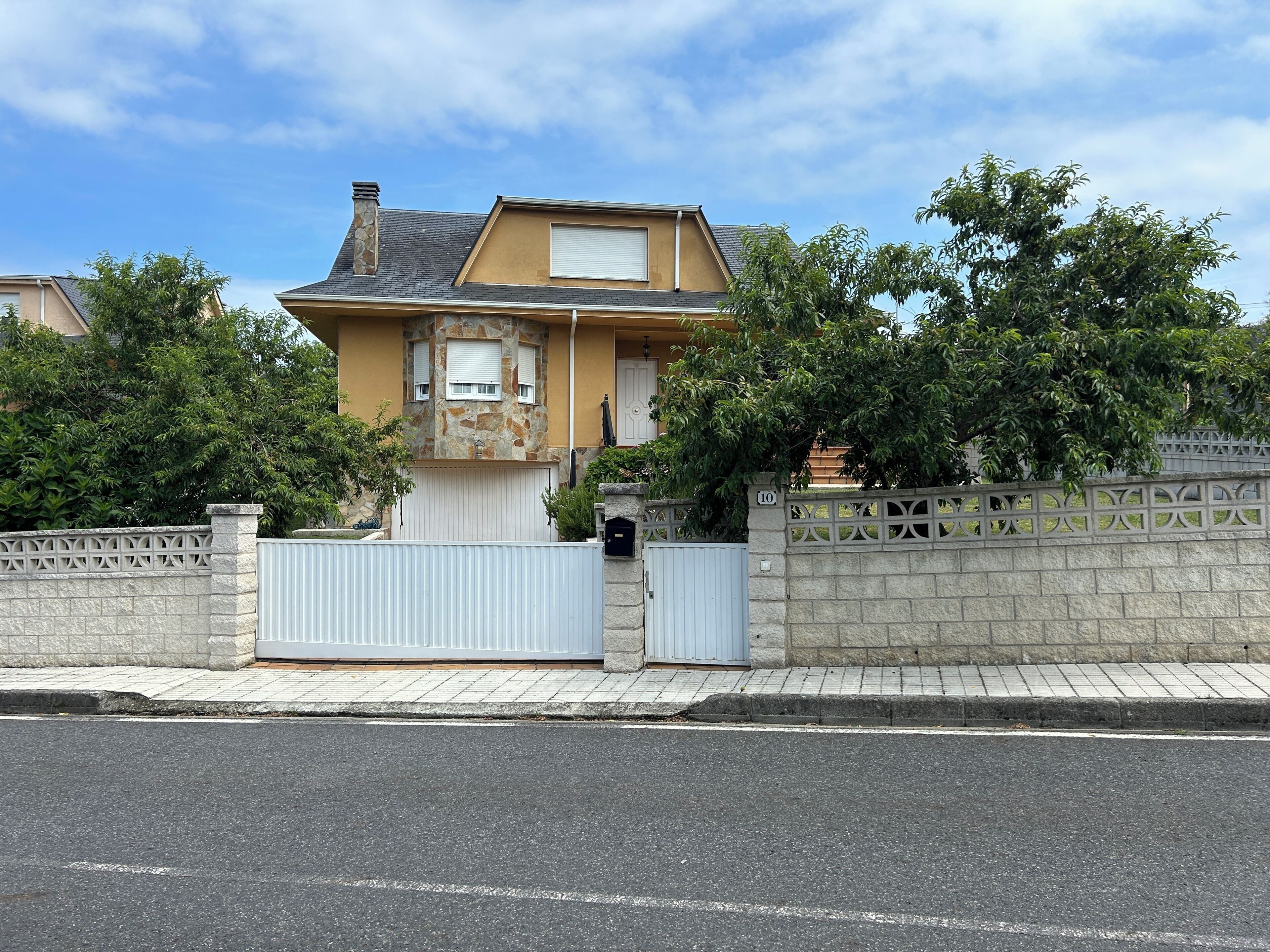 A residential house with a stone facade, a gated entrance, and a clear sky.