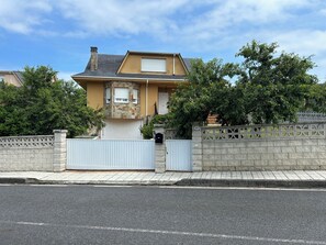 Una casa residencial con fachada de piedra, entrada protegida por un portón y cielo despejado.