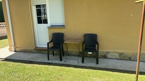 A patio with two chairs and a small table against a yellow wall, a door with blinds, and a wall-mounted light fixture. - Family home with a garden: Beach, mountains, and pets welcome (Garage included) (La Caridad)