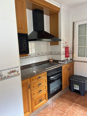 A kitchen with wooden cabinets, a black range hood, a microwave, a stove, and a trash bin.