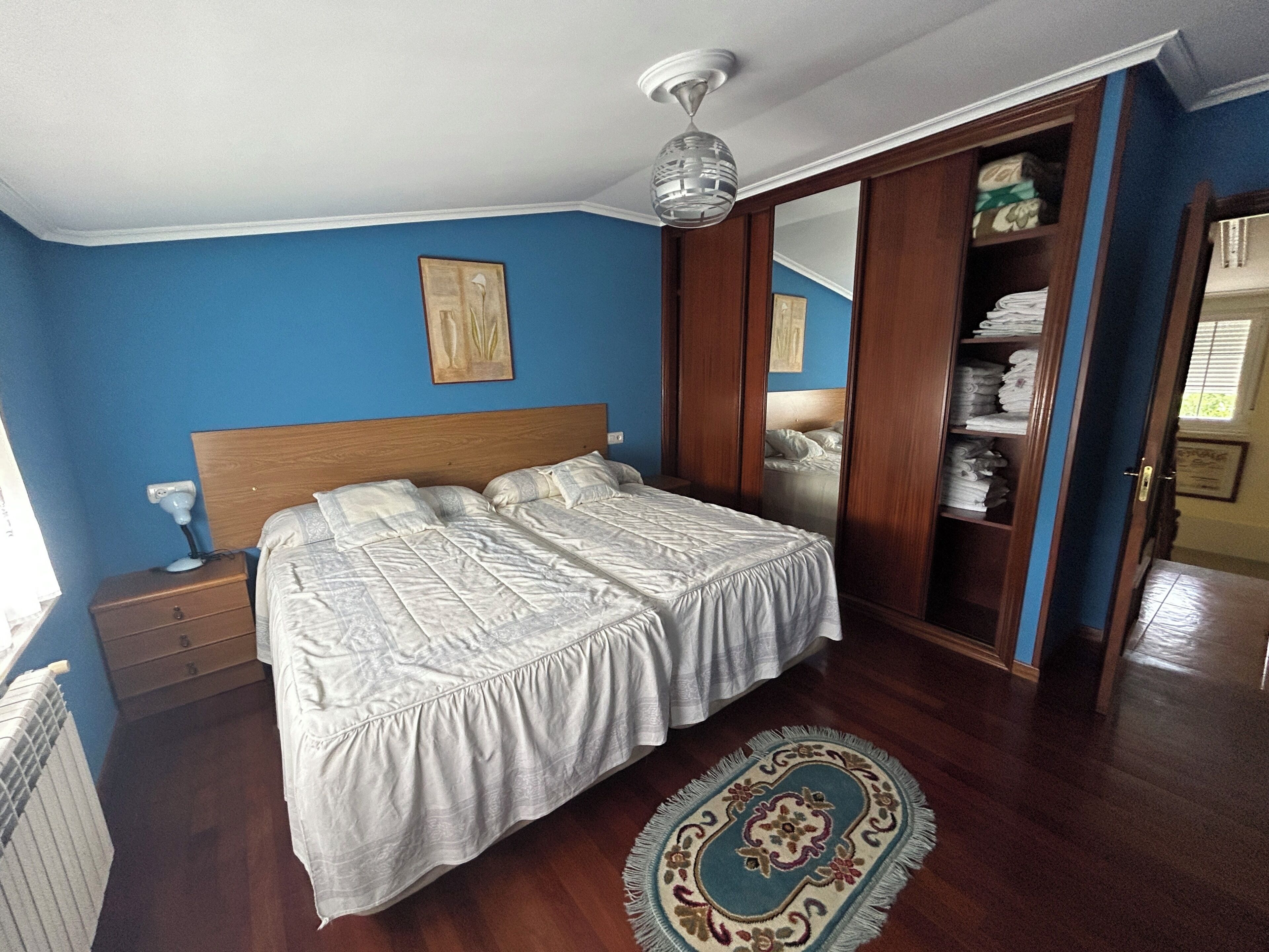 Een slaapkamer met een tweepersoonsbed, nachtkastje, bureau, stoel, kledingkast en plafondventilator.