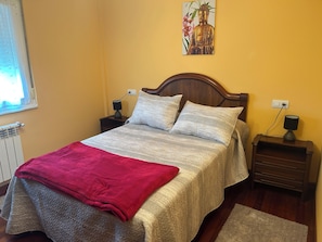 A bedroom with a bed, two bedside tables, a nightstand, a radiator, and a window.