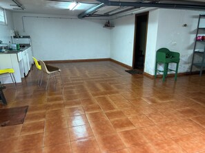 A room with a tiled floor, a kitchen area with white cabinets, a yellow chair, and a green chair.