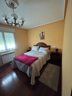 A bedroom with a bed, bedside tables, a nightstand, a radiator, a window with curtains, and a chandelier. - Family home with a garden: Beach, mountains, and pets welcome (Garage included) (La Caridad)