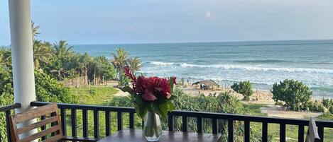 A wooden table and chairs on a balcony with a view of the ocean.
