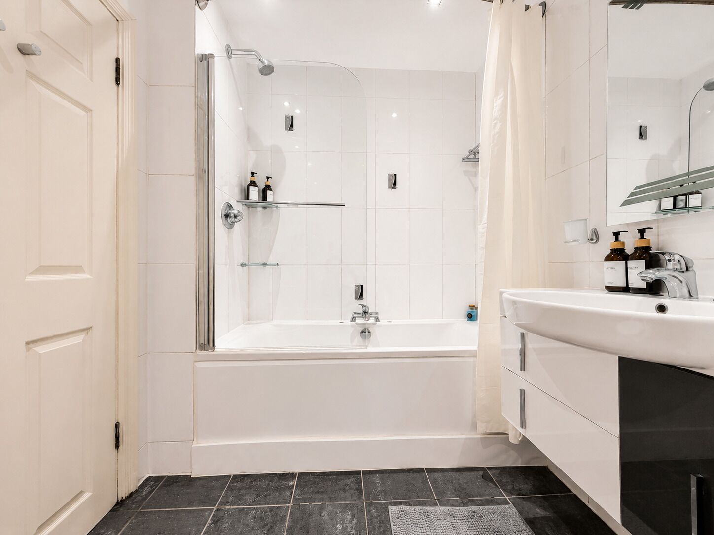 A modern bathroom with a glass-enclosed shower, a white bathtub, and a vanity with a mirror.