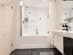 Un baño moderno con ducha envuelta en vidrio, una bañera blanca y un tocador con espejo.