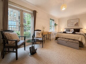 A bedroom with a bed, two chairs, a small table, and a window with curtains. - Central Garden Townhouse near Oxford St and SoHo (London)