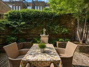 A patio with wicker furniture and a patterned tablecloth, surrounded by a brick wall and greenery. - Central Garden Townhouse near Oxford St and SoHo (London)