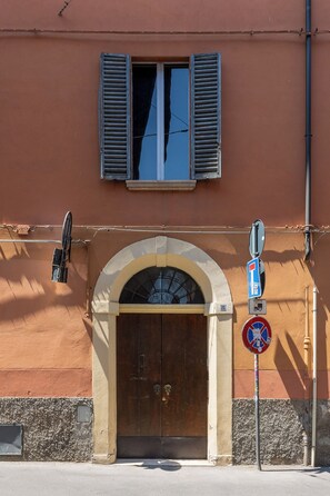 Ein Gebäude mit einem großen Bogenportal, einem Fenster mit Rollläden und einem Straßenschild.