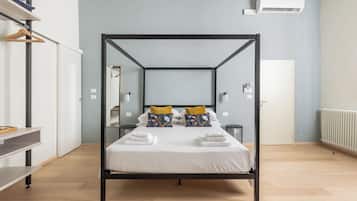 Een hemelbed met witte lakens en decoratieve kussens, een nachtkastje met dienblad, een garderobe en een radiator.