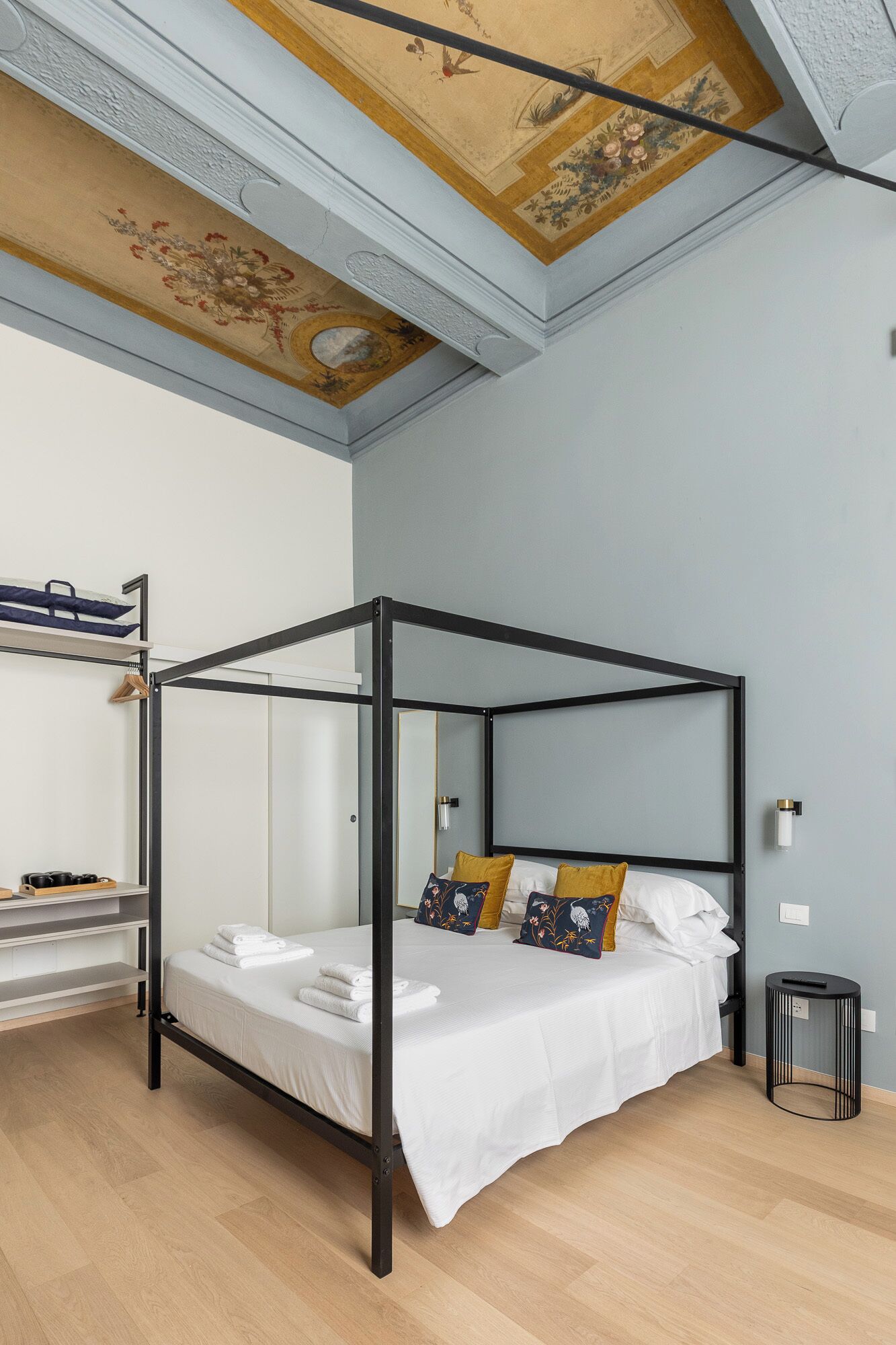 A modern bedroom with a four-poster bed, a wooden floor, and a decorative ceiling.