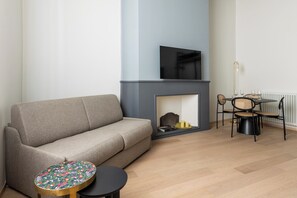 A modern living room with a grey sofa, a small round table with a colorful floral pattern, a fireplace, and a dining area with chairs and a table.