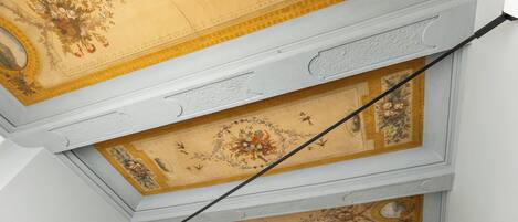 A ceiling with intricate floral and geometric patterns, a visible structural beam, and a section of a wall with a decorative molding.