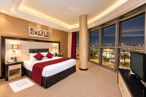 A hotel room with a large bed, a nightstand, a TV, and a city view through the window. - Rand By Wandalus Hotel (Riyadh)