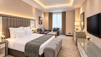 Habitación de hotel con una cama grande, un sofá, un escritorio, un televisor y una ventana con cortinas.