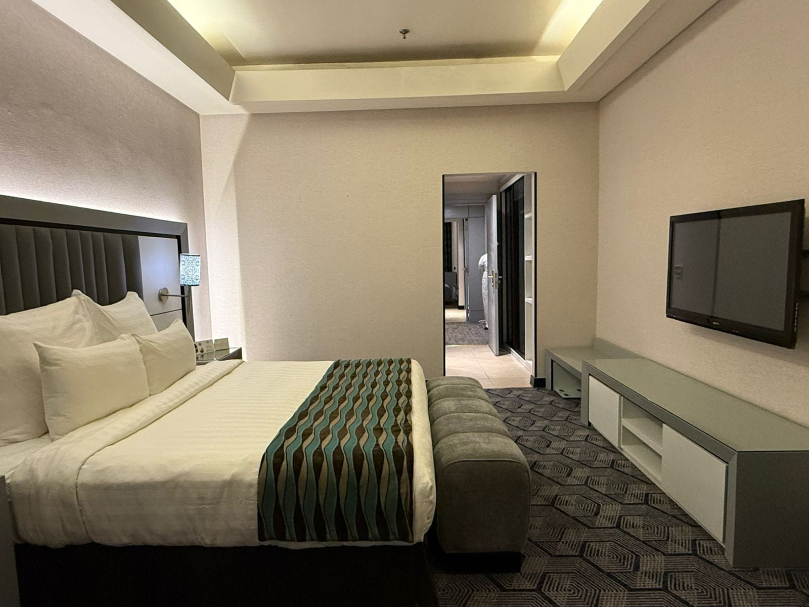 A hotel room with a bed, a bench, a television, and a desk.