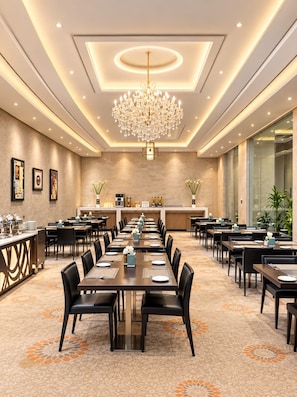 A spacious hotel dining area with long tables, chairs, a central chandelier, and a buffet counter. - Rand By Wandalus Hotel (Riyadh)